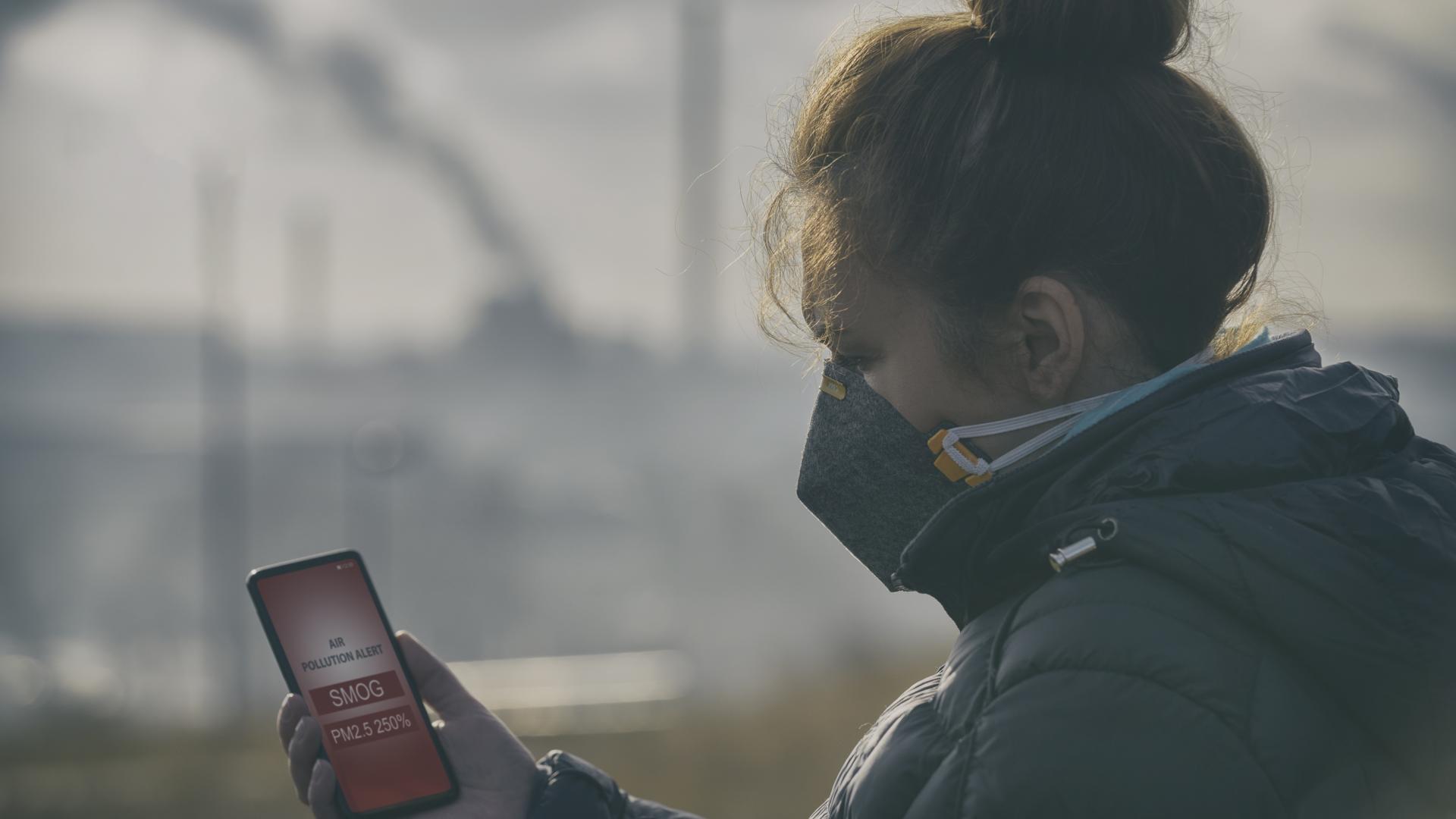 Woman wearing an air pollution mask and checking an air pollution app on her phone.