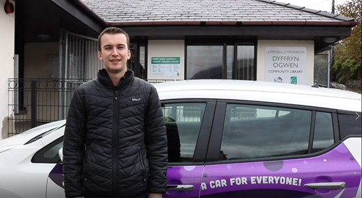 Photo of Rhys Gwilym standing in front of purple and white community car