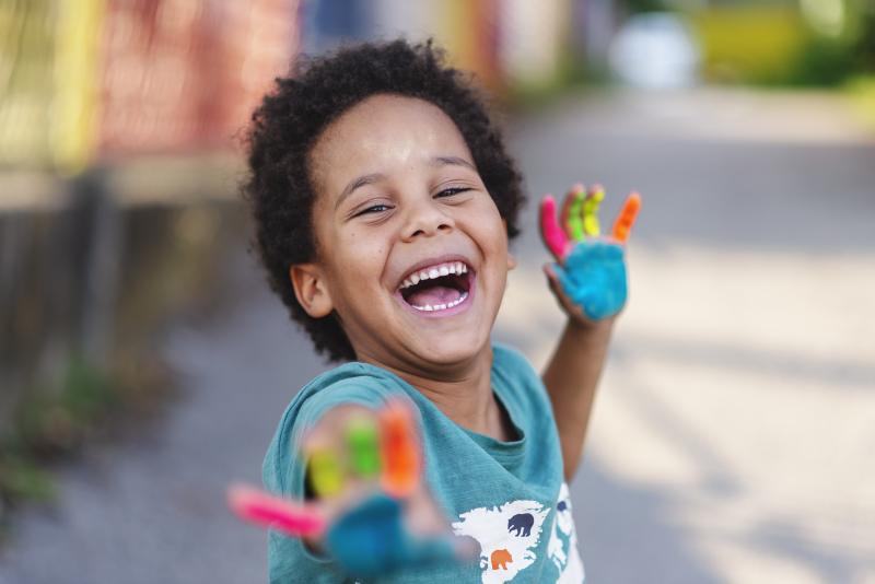 Beautiful child  waves painted hands and laughs into camera