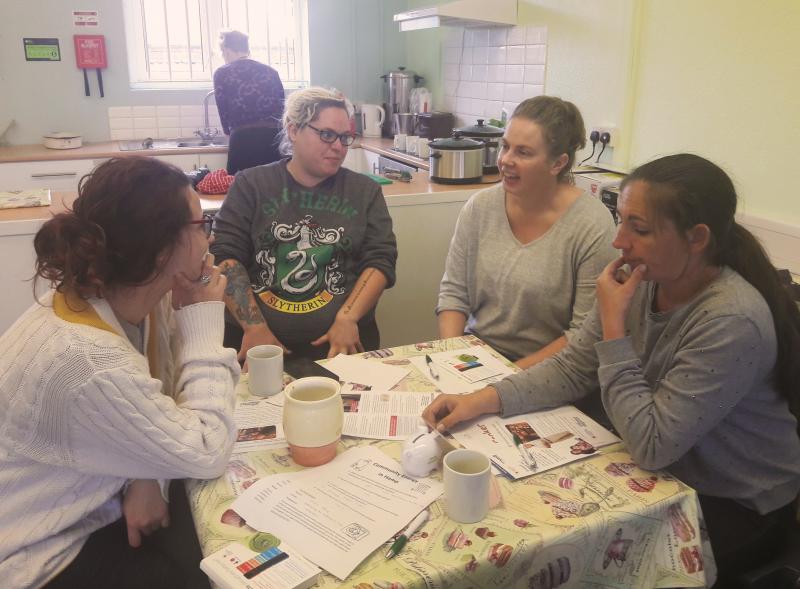 4 women sitting at table in kitchen discussing energy advice leaflets
