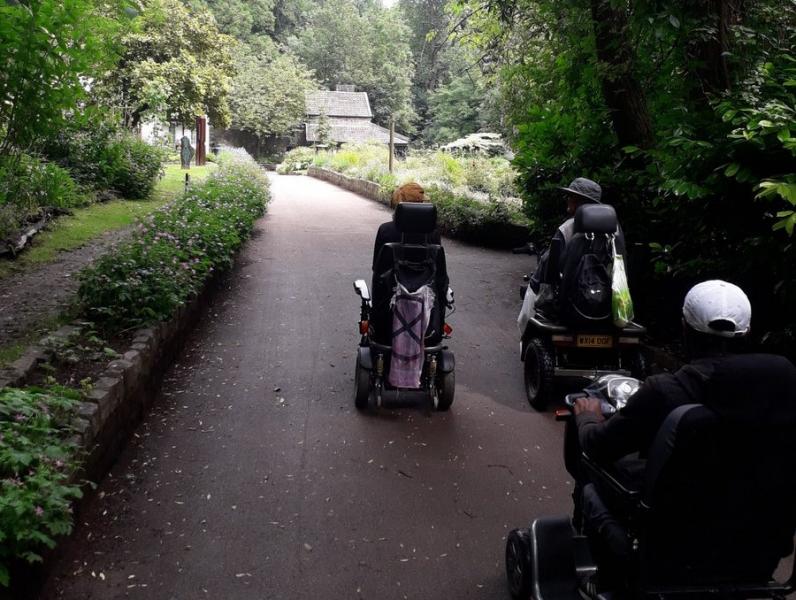 Backview of electric wheelchair users heading away from viewer on a road in a parki