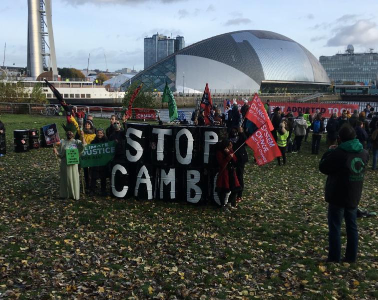 Activists standing around Stop Cambo oil drum installation, with COP26 venue in the background