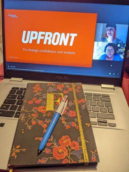 UPFRONT logo on computer screen, notebook and pencil on desk in foreground