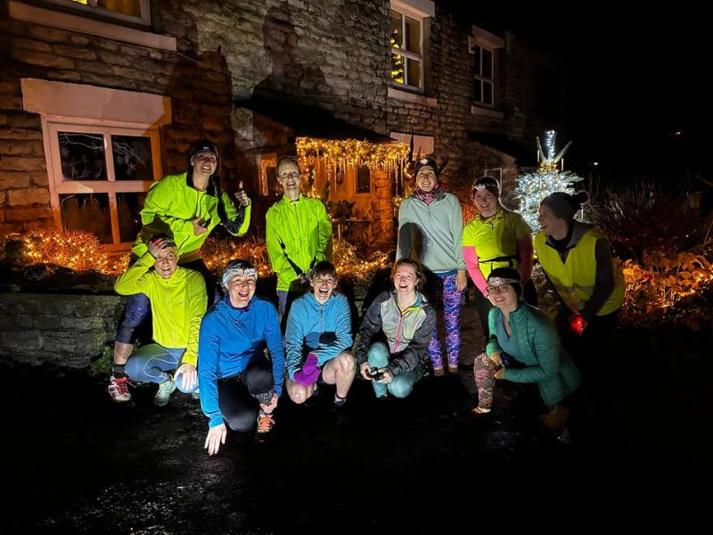 Night shot of a group of women in outdoor running gear and head torches laughing together outside Derbyshire pub