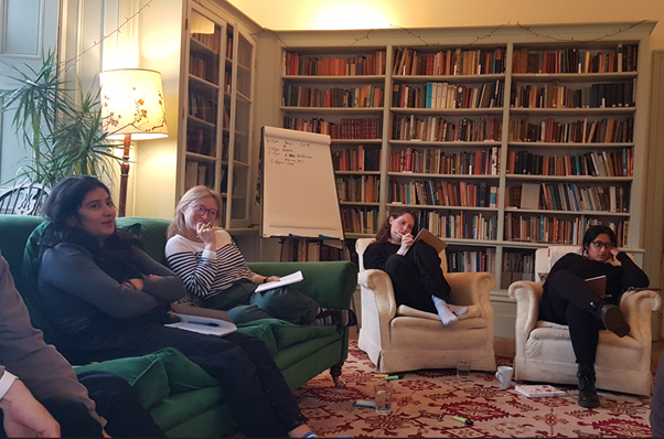 4 people sit in a circle on easy chairs in a high ceilinged library