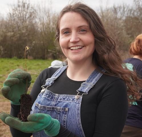 head and shoulders shot of Fenella Corrin, holding a plant in her gloved hands