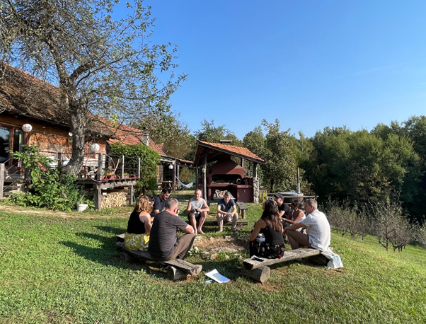 People sitting on grass in a circle, Croatian house and country landcsape in background