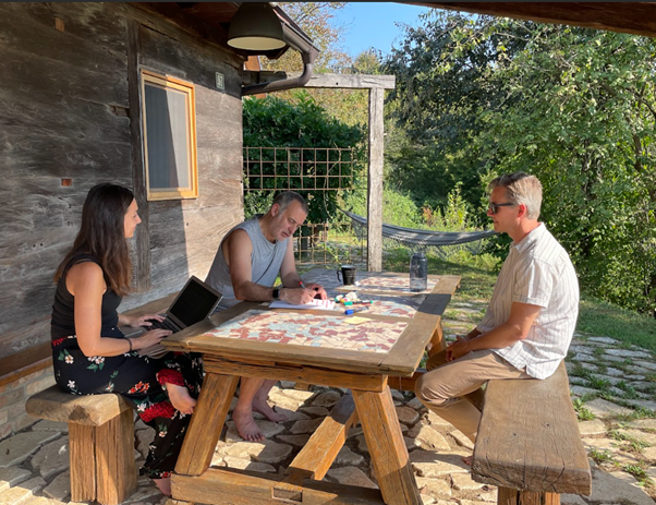 3 people sitting around a wooden table outside house at Croatian retreat