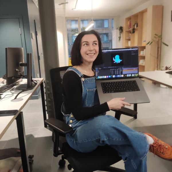 Woman sitting on office chair holding up laptop showing OctopAI logo on screen