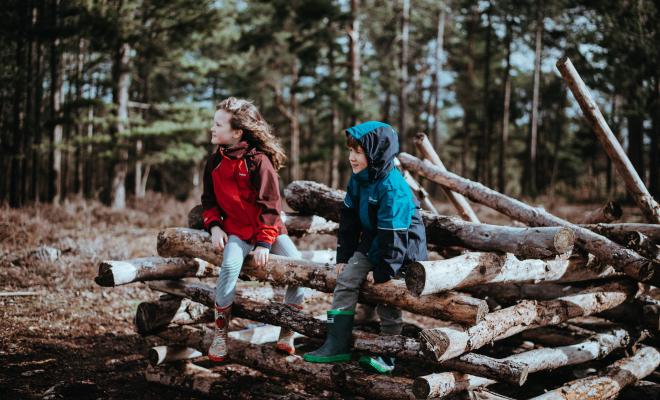 two kids sitting on logs with trees in background