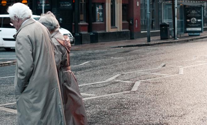 Old people in rainwear crossing street, car in background