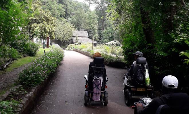 backview of electric wheelchair users heading away from viewer on a road in a parki