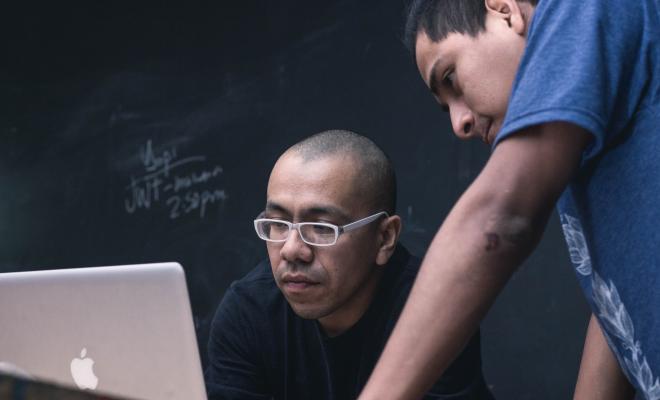 Two men conferring whilst studying something n an open laptop