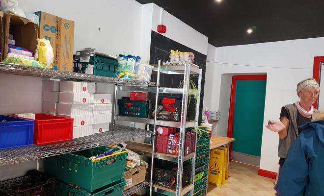 Shelves stocked with dried and canned food, woman in background