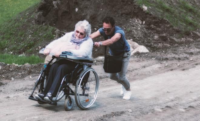Man pushing elderly lady in wheelchair up a steep slope
