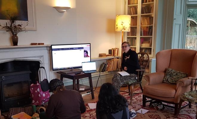 2 women participants in immersion Lab with backs to camera listen to online tutorial with facilitator explaining something