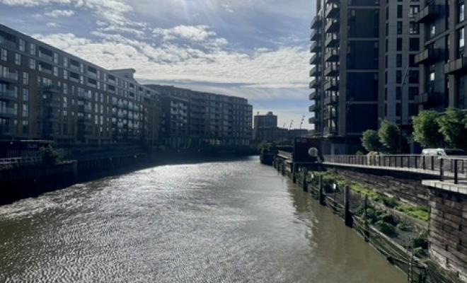 View of Thames with high buildings on both sides, greenery growing by riverside path
