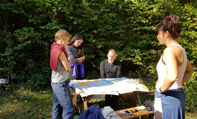 4 people standing in sunshine around a table looking at flip charts with post-its