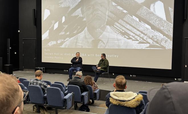 Ben Wheatley and interviewer are on a stage in front of a screen talking to an audience during a Q&A