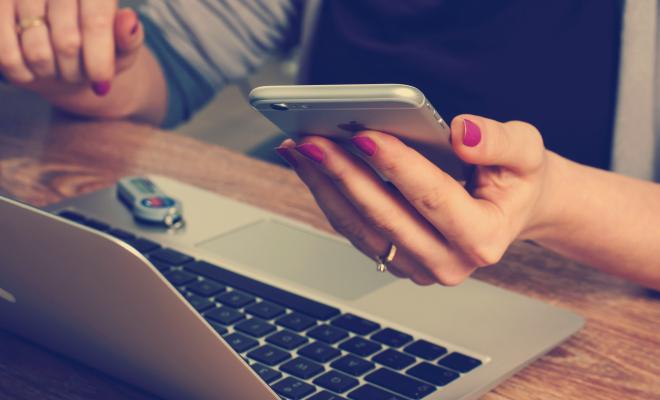 Hand holding mobile by open laptop